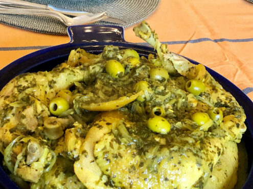 A dish of lemony chicken pieces with herbs and olives.