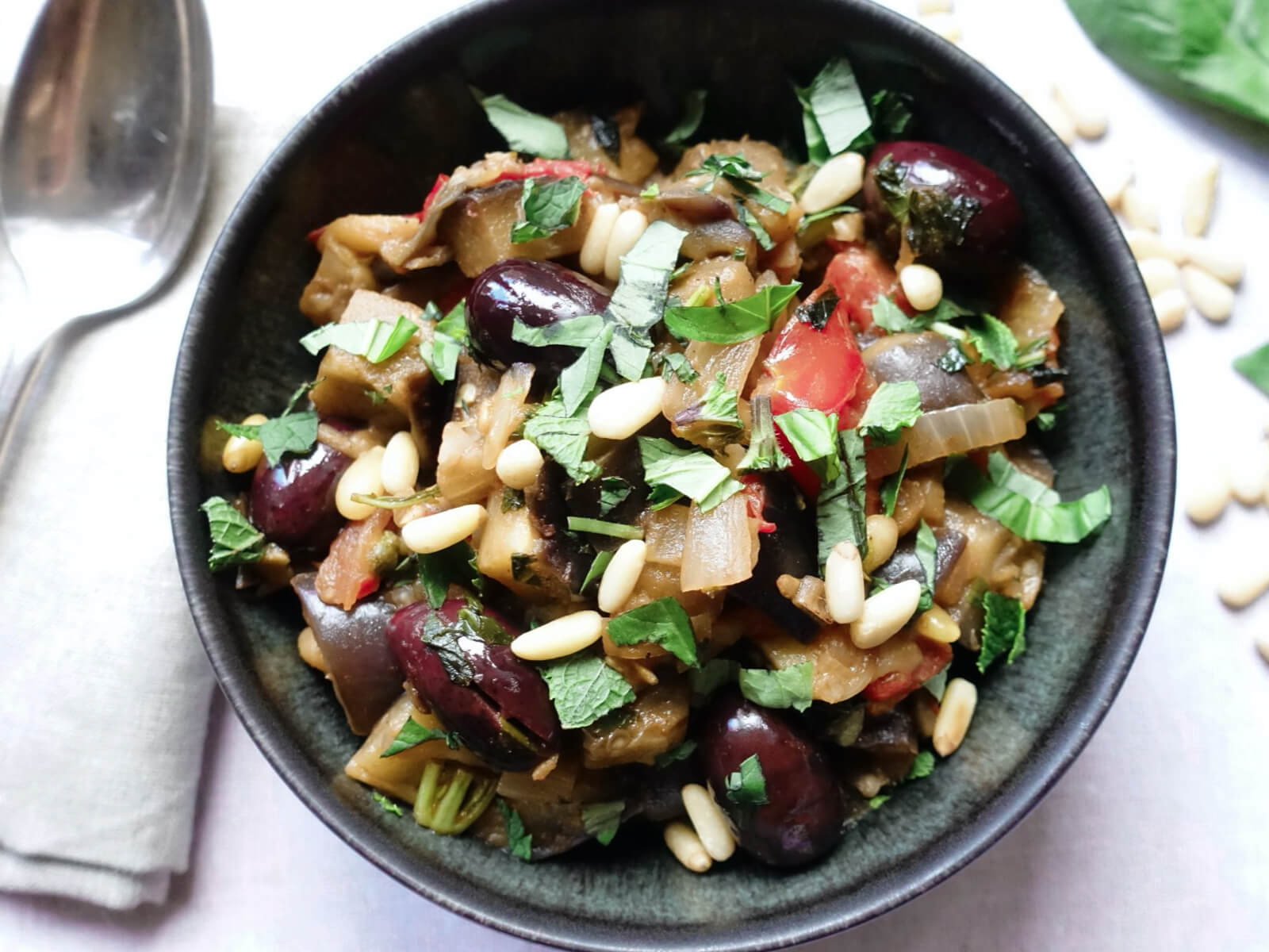 A bowl of eggplants with pine nuts and herbs on top.