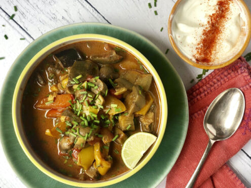 A bowl of spicy vegetables with chives on top and a slice of lime