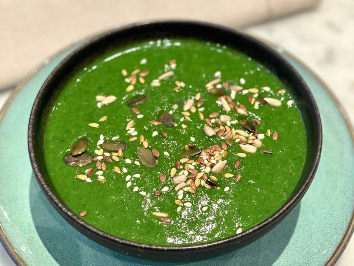 A bowl of vibrant green spinach and zucchini soup topped with seeds. A powerhouse recipe that reduces inflammation and helps with mental health issues.