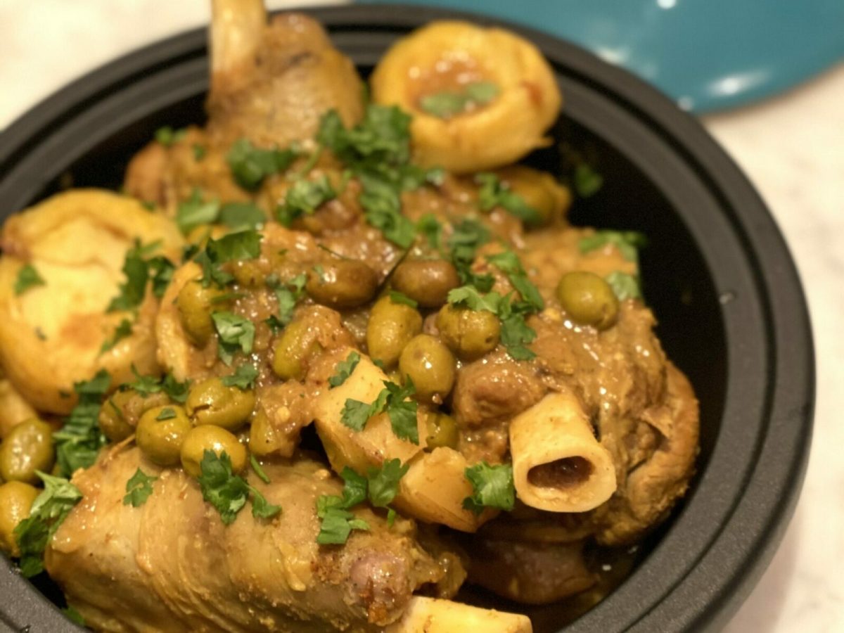 A pan with lamb, artichokes, olives and lemons with chopped green herbs on top.