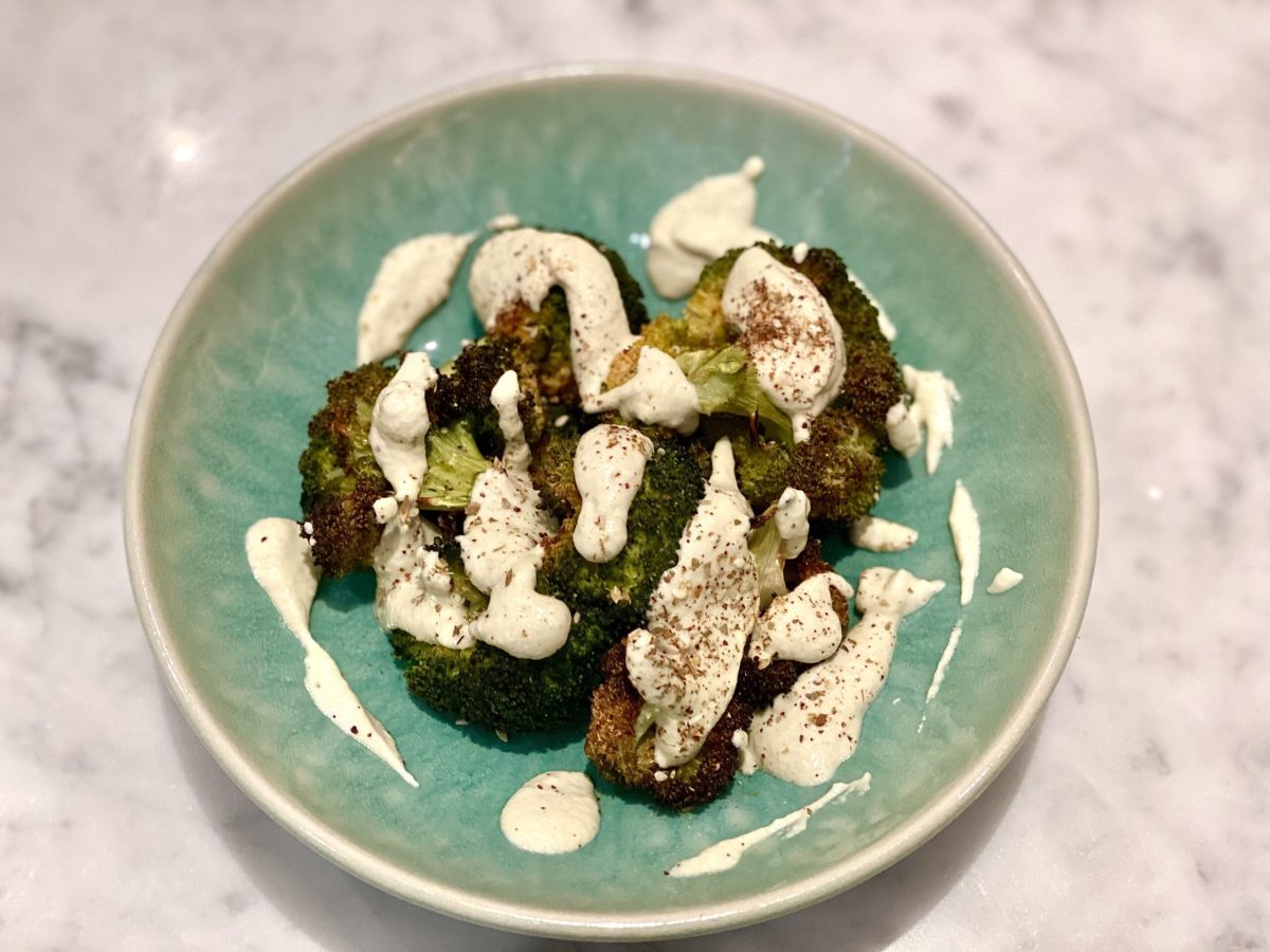 A plate of broccoli with tahini sauce drizzled over the top of it.