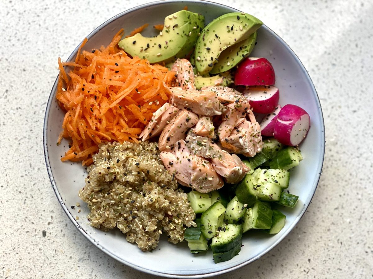 A bowl of avocado, grated carrot, other veggies, quinoa and salmon in a bowl.
