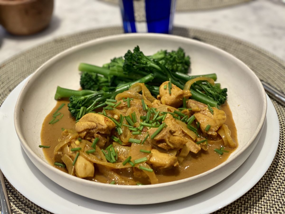 A bowl of chicken in a turmeric gravy served with broccoli.