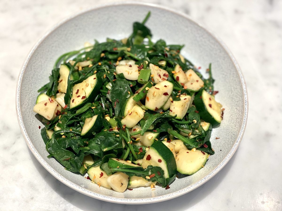 A dish of sautéed spinach and zucchini with some flakes of seasoning on top.