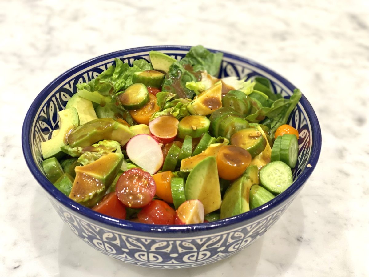A bowl of chopped up lettuce, tomatoes, avocado and radish with a dressing on, showcasing a salad for lowering inflammation.