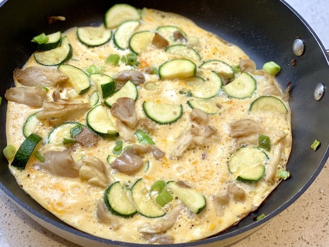 An omelet with sliced zucchini and mushrooms in a pan.