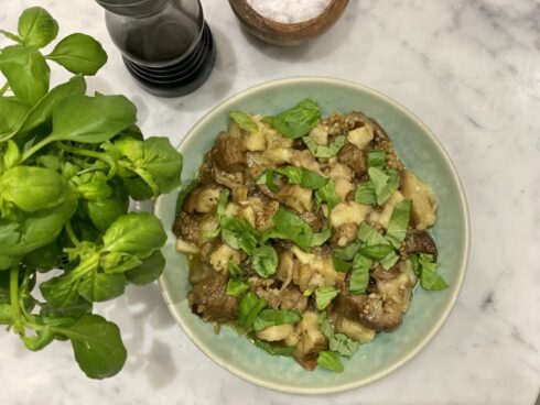 A bowl of eggplant salad with chopped basil on top.