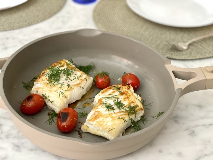 Two loins of cod seared in a pan with cherry tomatoes.