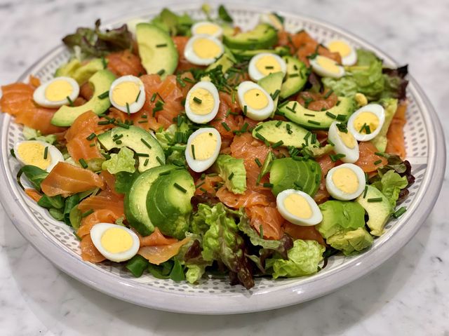 A colourful smoked salmon recipe to reduce inflammation: a large bowl of smoked salmon salad with quails' eggs, avocado, lamb's lettuce and parsley.