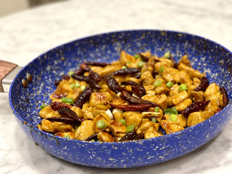 A pan containing cooked chicken and chilies, decorated with chopped scallions - a recipe from a low-inflammation lifestyle plan.