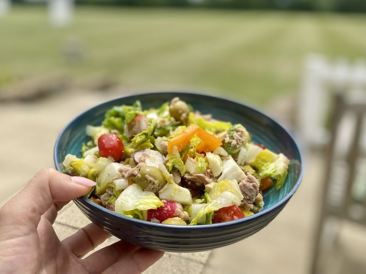 A bowl of lettuce, radishes, fish, fruit and other items, making a mixed salad.