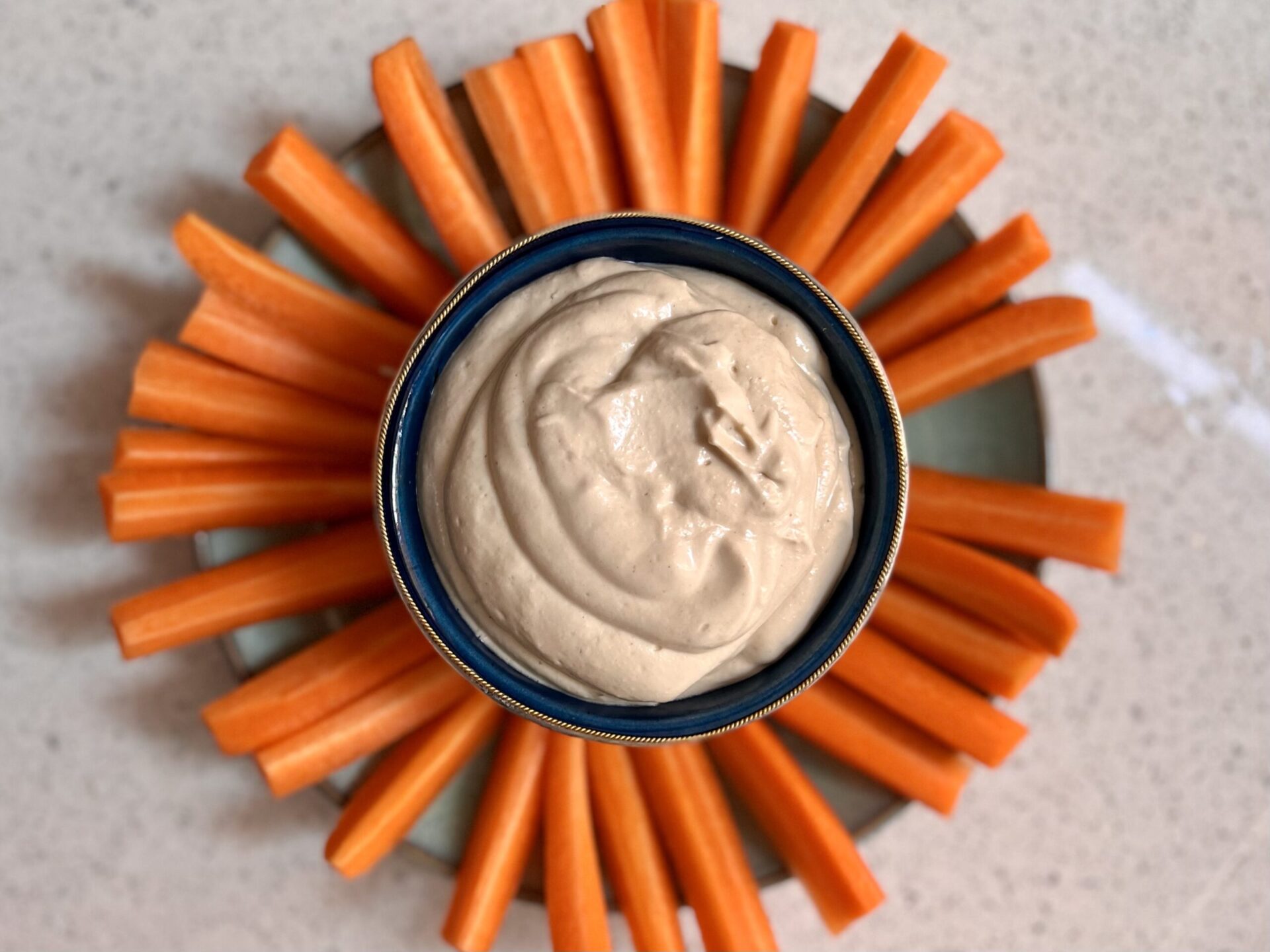 A plate of carrot sticks with a pot of tahini dip in the middle.