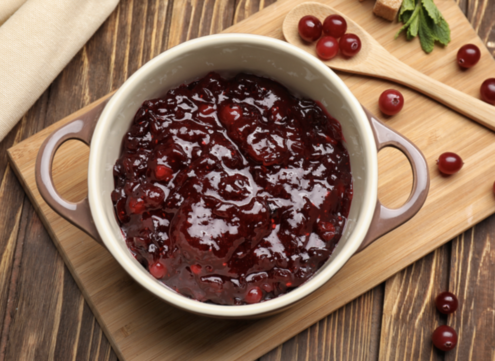 A dish of cranberry sauce on a wooden chopping board with a spoon of cranberries by the side.