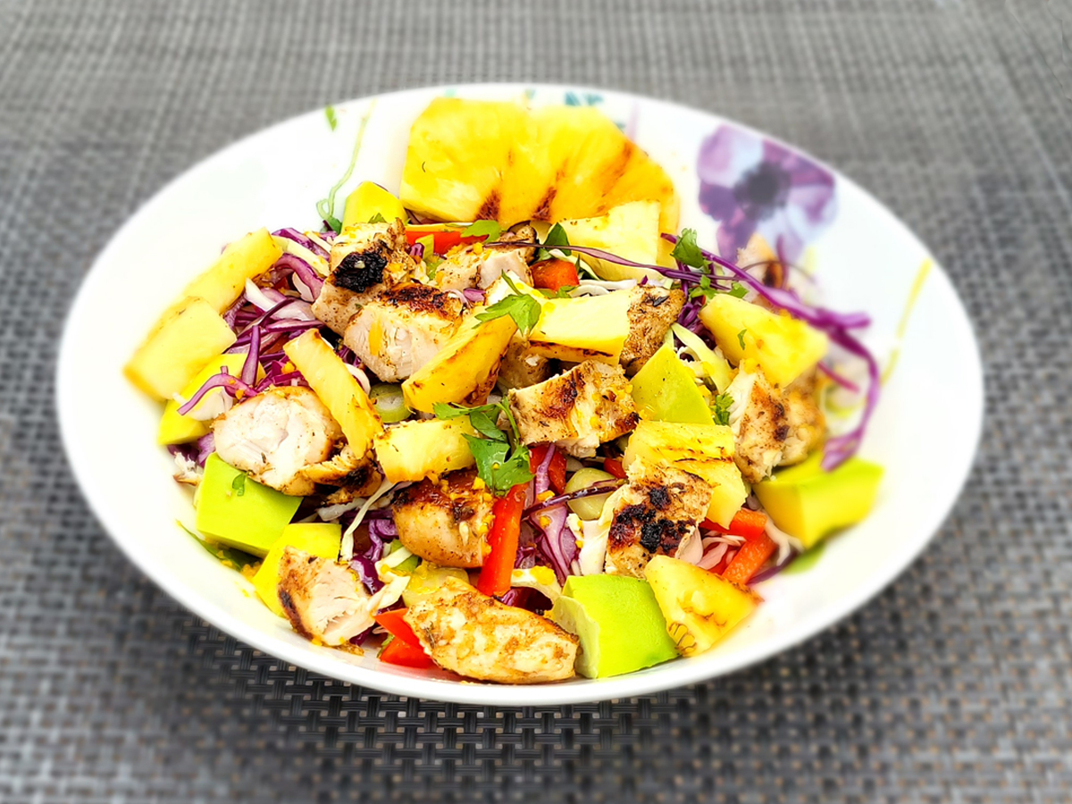 A bowl of chicken, peppers, onions, pineapple, and other colourful vegetables, as part of a Caribbean meal.