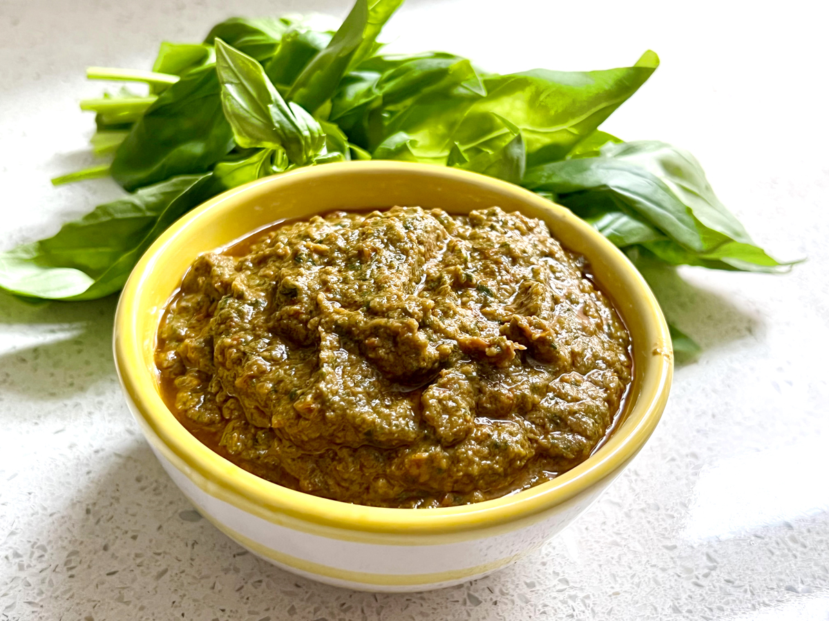 A yellow bowl full of sun-dried tomato pesto with basil leaves at the side.