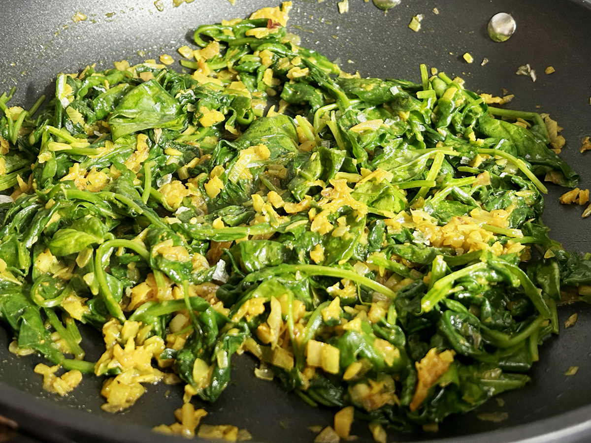 A pan of stir-fried spinach with a splash of orange from turmeric.