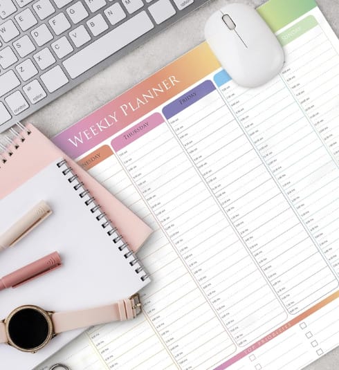 Weekly planner on desk by keyboard, pen, notebook and mouse