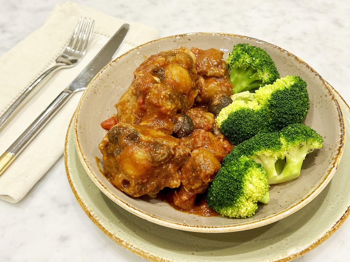 Oxtail, tomato and mushrooms stew on a plate with cooked broocoli