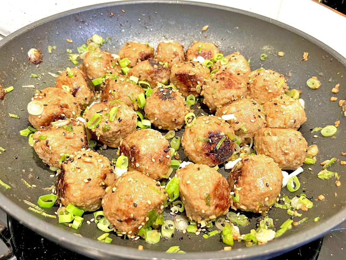 Asian style meatballs in a frying pan decorated with spring onions/scallions