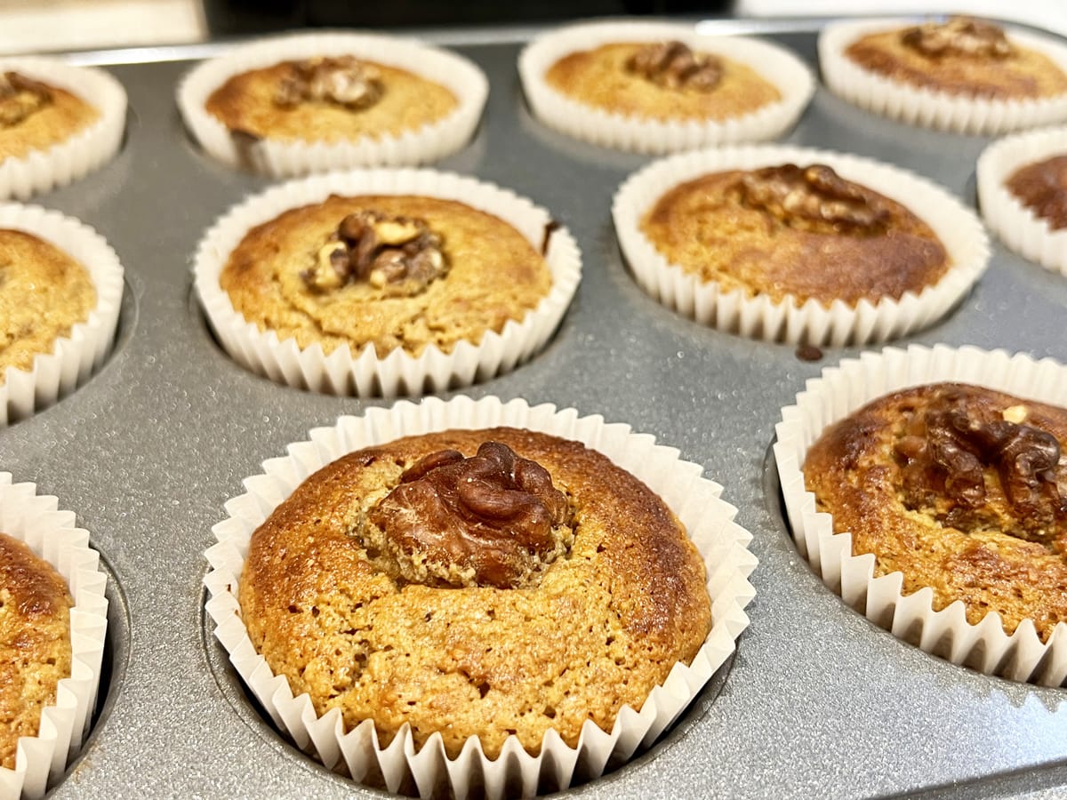 muffin tray with banana muffins decorated with a walnut piece