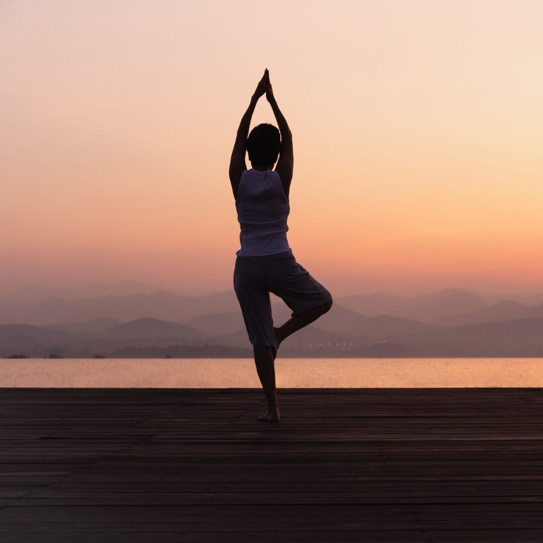 woman standing in tree pose by sunset promoting Cortisol Regulation