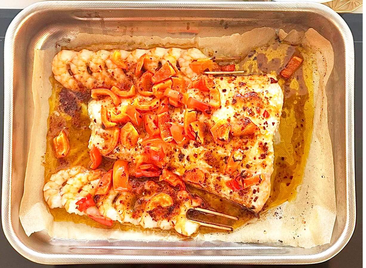 An oven dish filled with spicy tamarind salmon and prawns with lemon roasted red peppers.