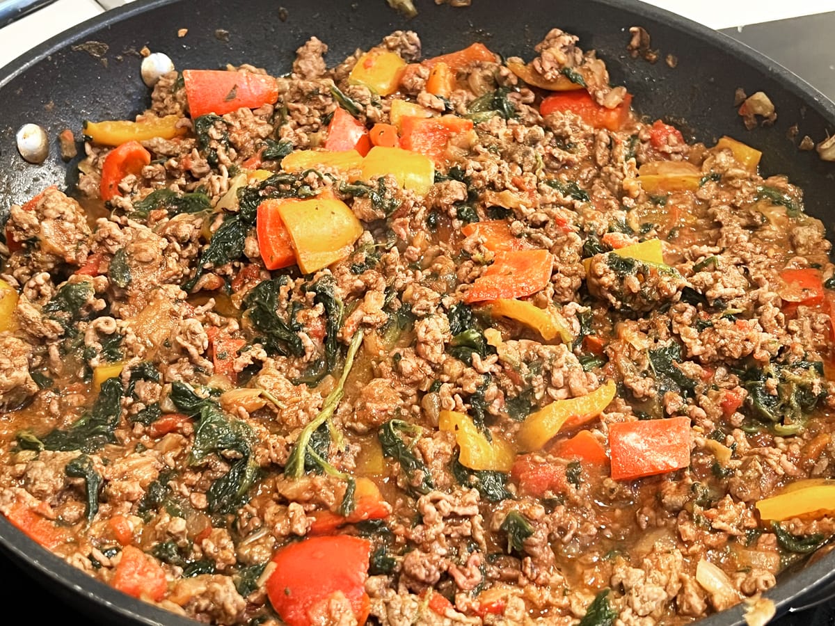 in a frying pan there is beef mince, red and orange bell peppers, wilted spinach and seasoning