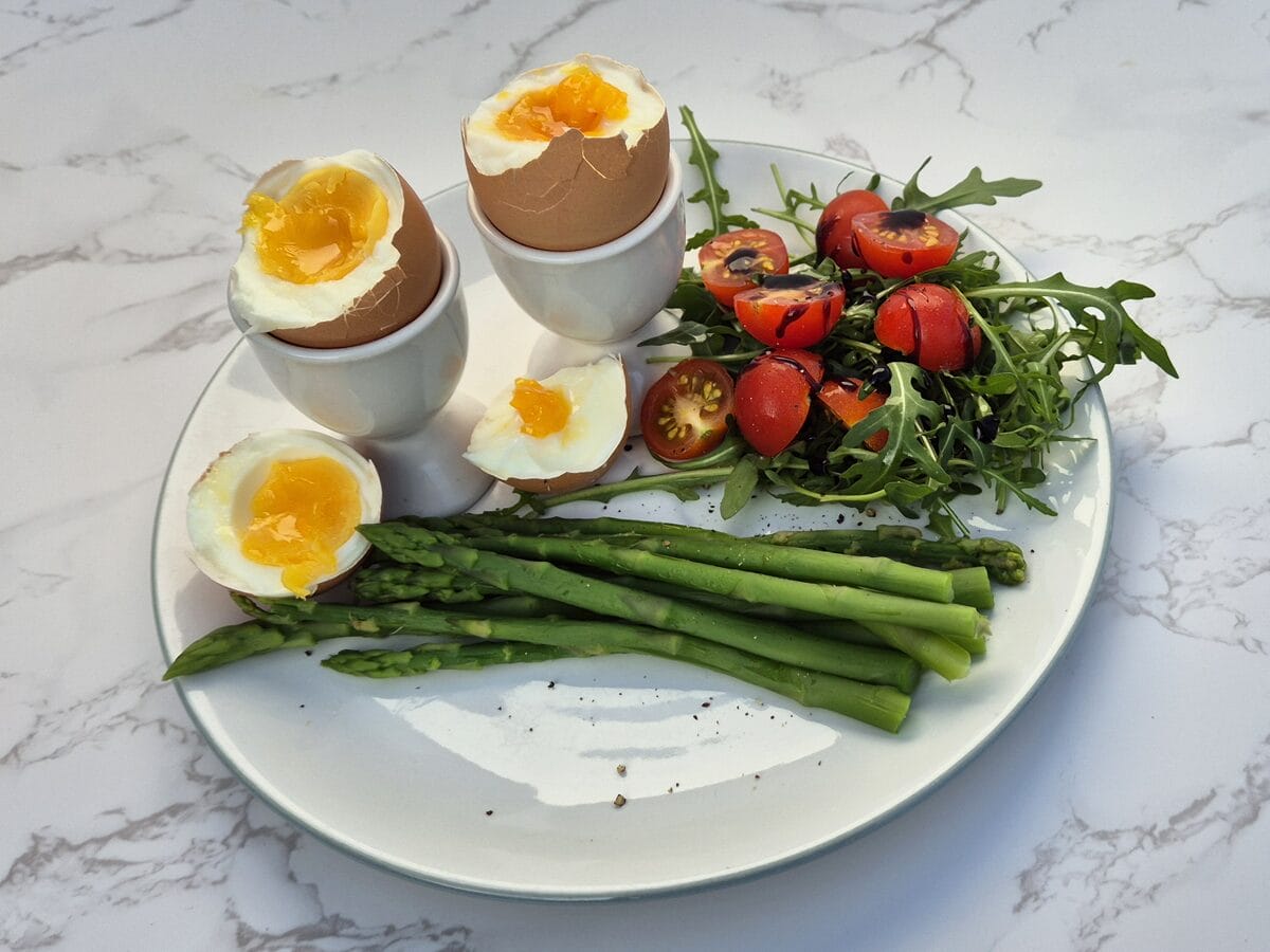 plate with soft boiled eggs and asparagus and side salad of rocket and cherry tomatoes