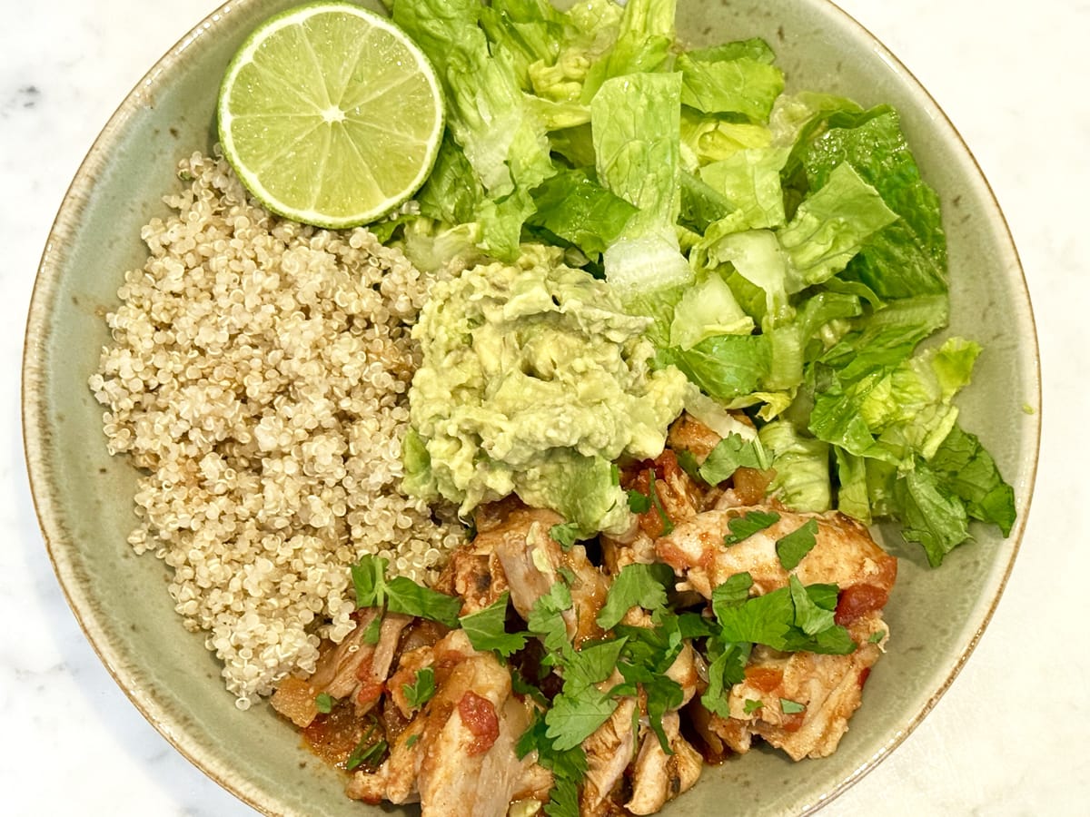slow cooker mexican chicken in a blow with quinoa, guacamole and garnished with lime and chopped cilantro