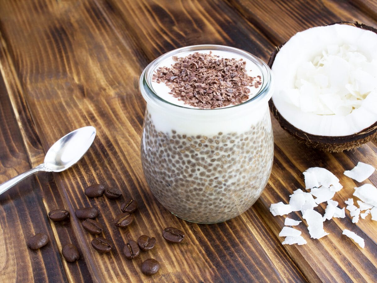 Tiramisu Chia Pudding dusted with chocolate shavings with a scattering of coffee beans and coconut on the side